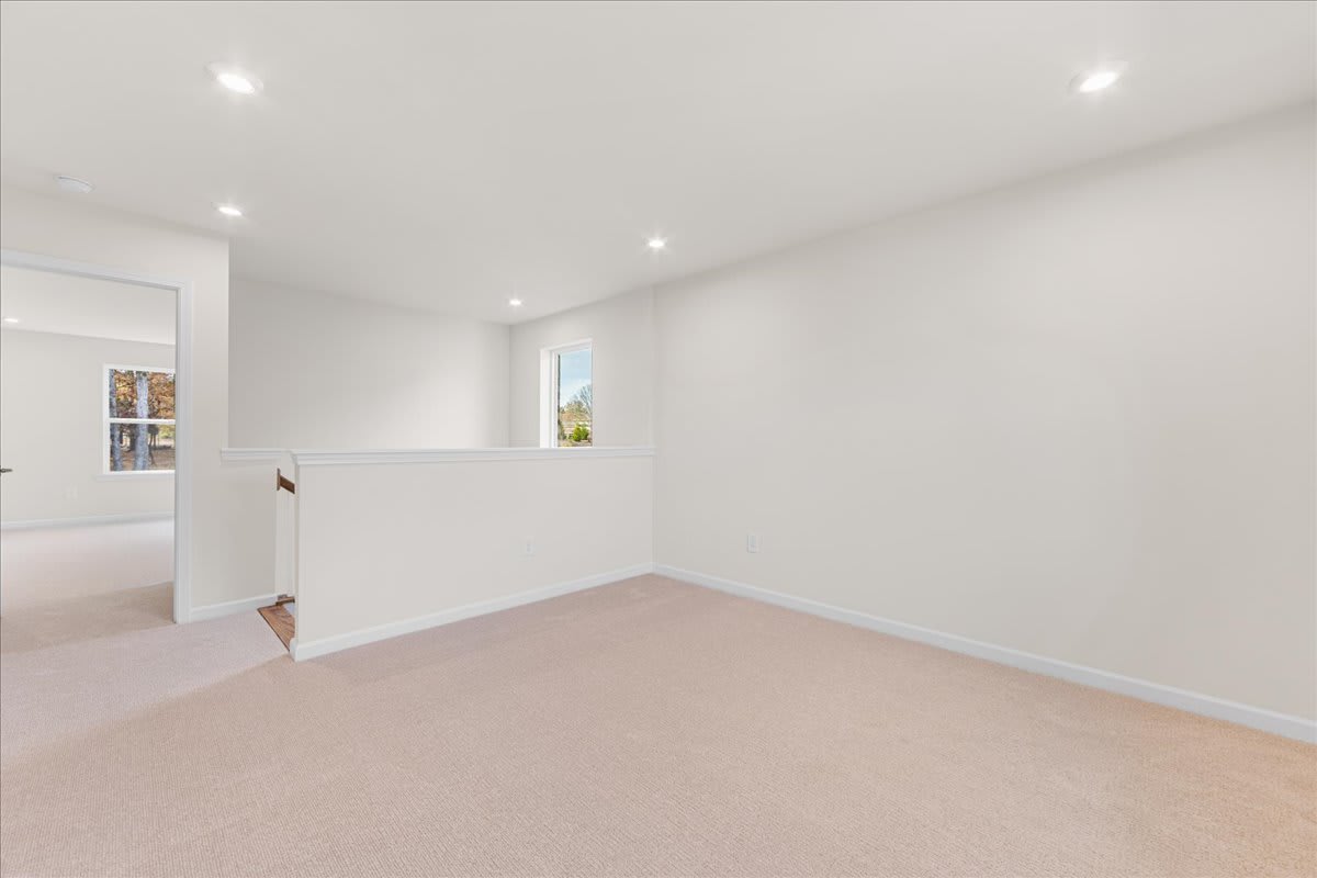 A bright, minimalist room with white walls, recessed lighting, and a beige carpeted floor.