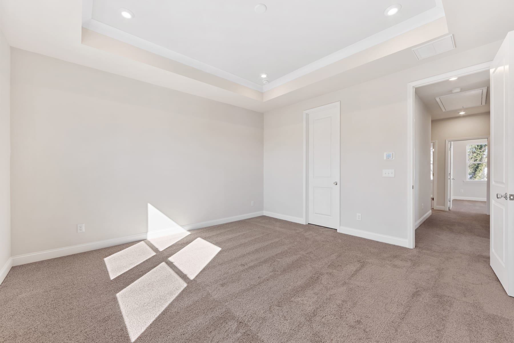 A spacious, well-lit room with white walls, a tray ceiling, and a carpeted floor, creating a clean and modern atmosphere.