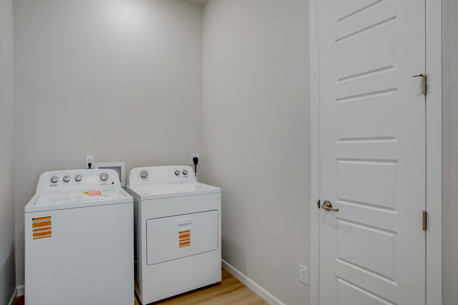 A small, white laundry room with a washer and dryer in the foreground and a white door in the background.
