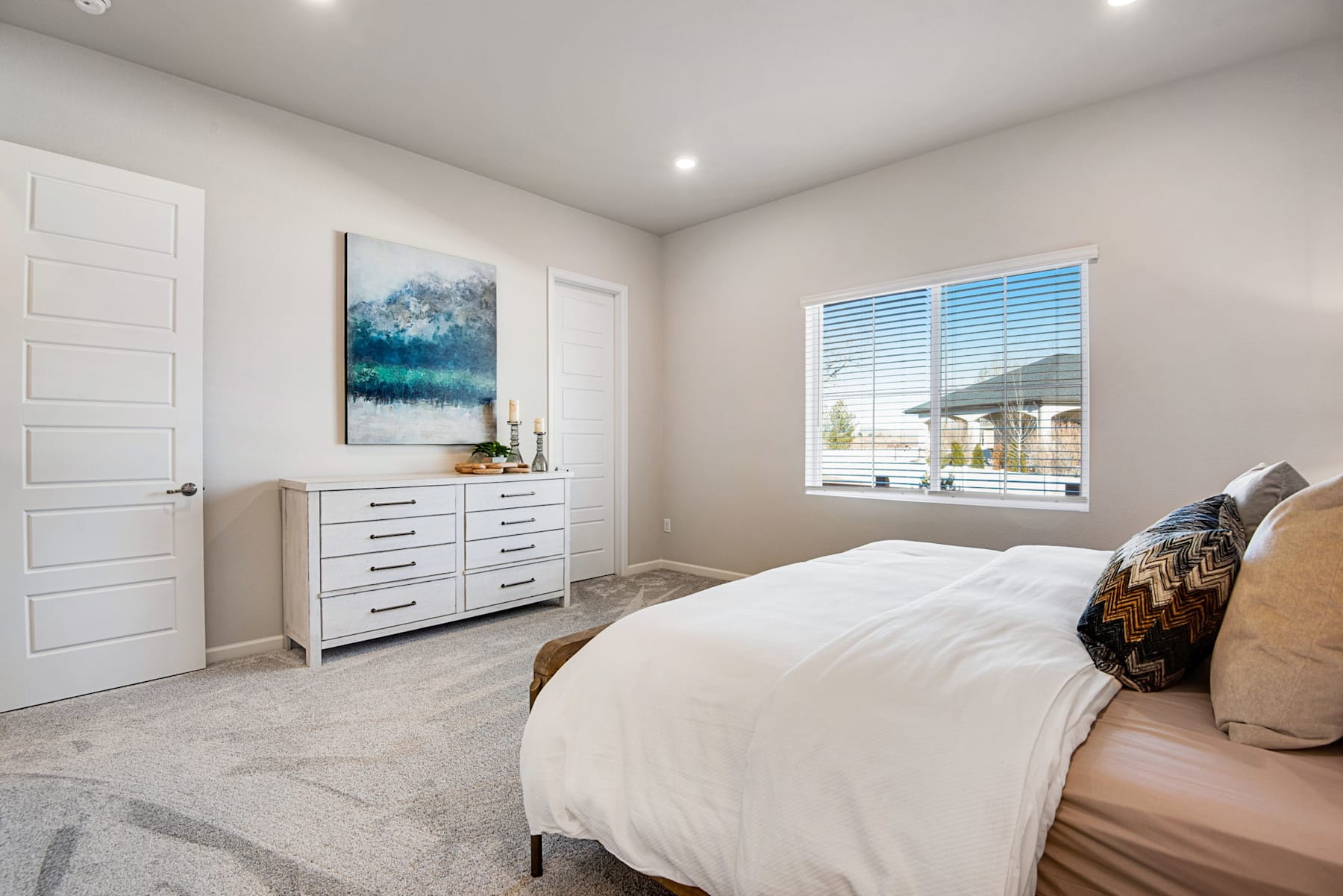 A spacious and well-lit bedroom with a large bed, a dresser, and a window overlooking a scenic outdoor view.