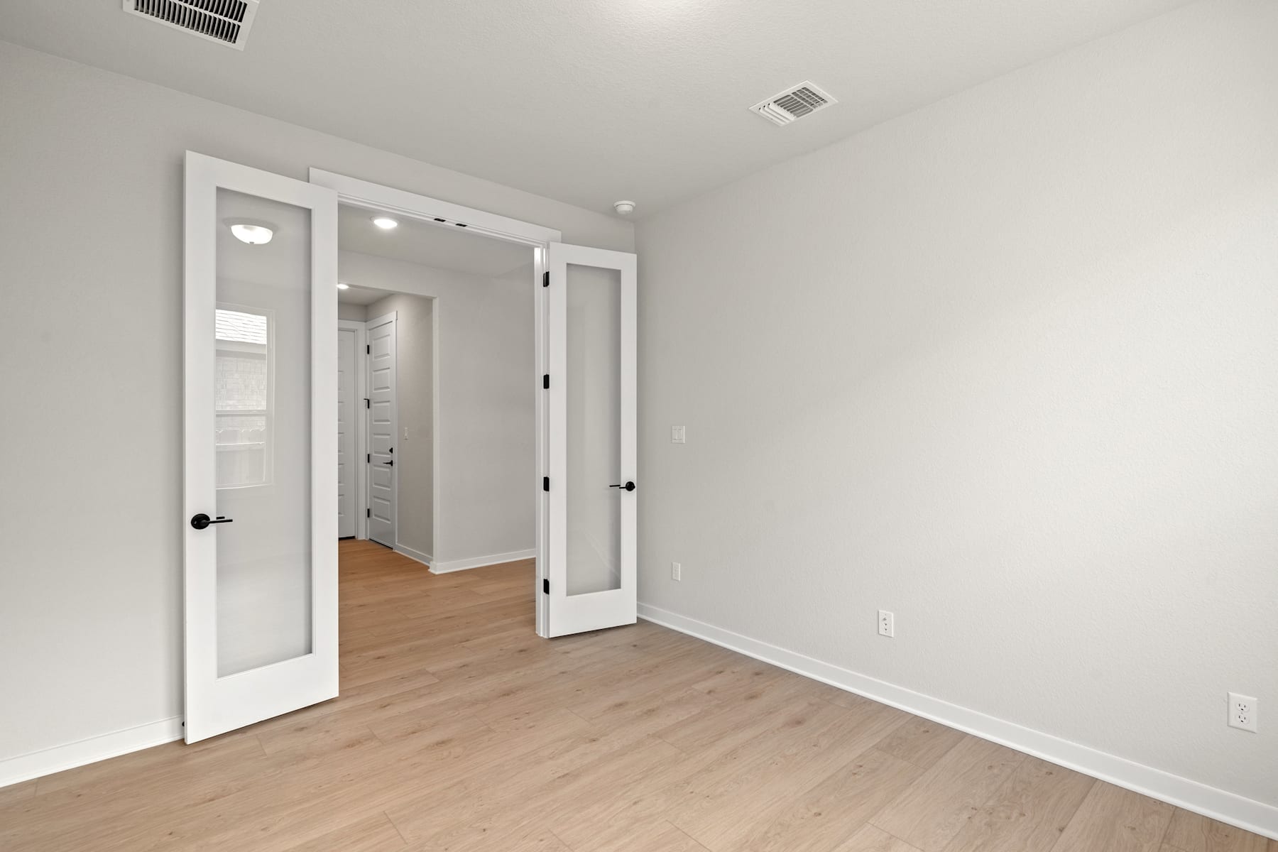 A spacious, minimalist room with white walls, wooden floors, and a closet with mirrored doors.