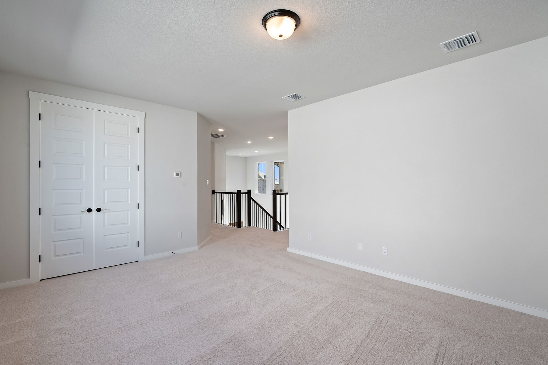 A bright, minimalist hallway with white walls, a wooden floor, and a ceiling light fixture, leading to a doorway.