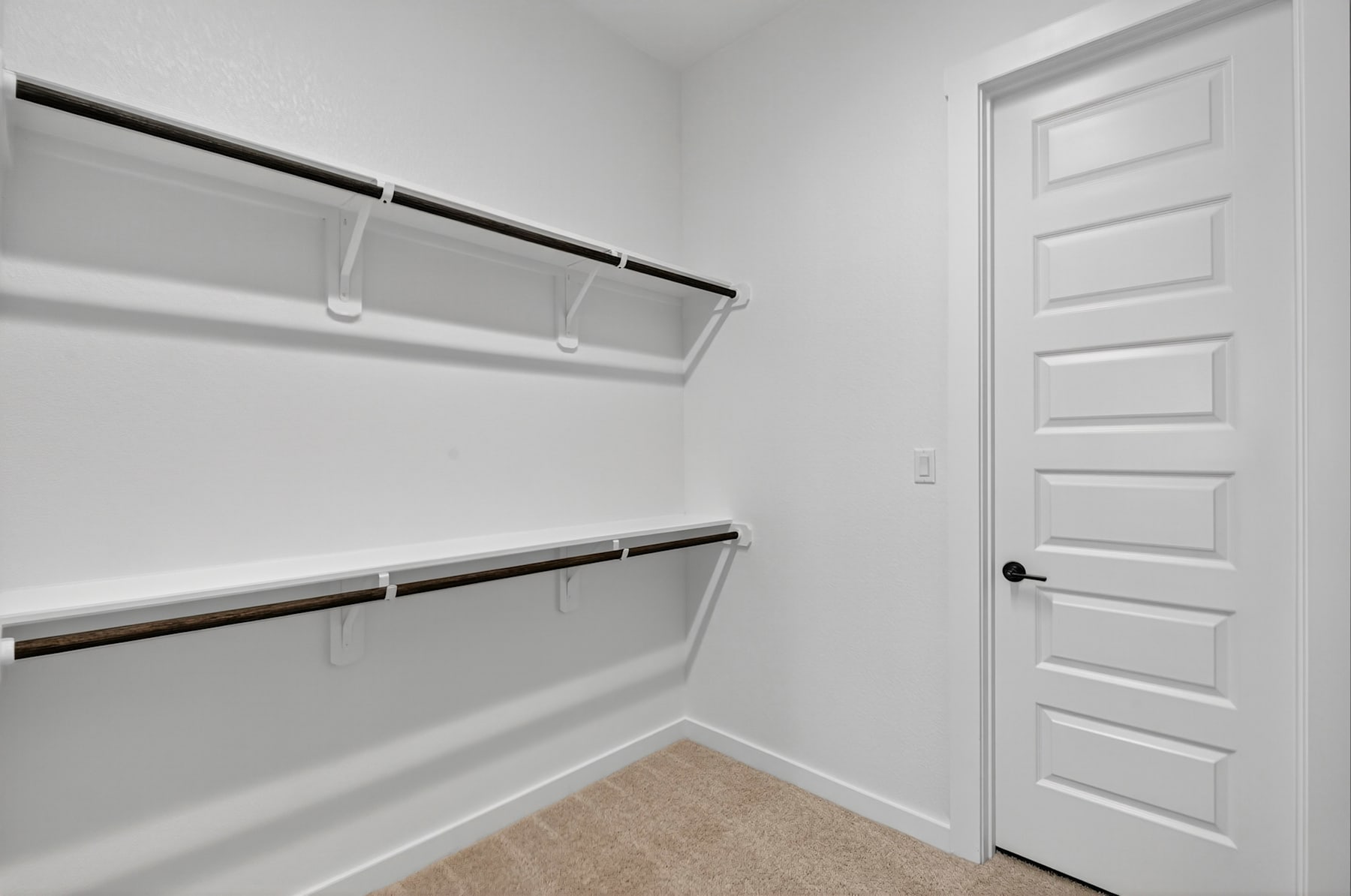 A simple, minimalist closet space with white walls, shelves, and a closed white door in the background.