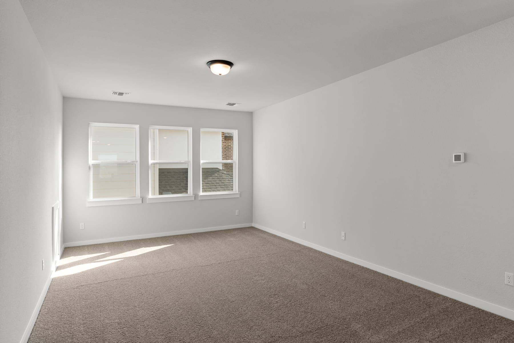 A sparsely furnished room with white walls, a ceiling light fixture, and a carpeted floor.