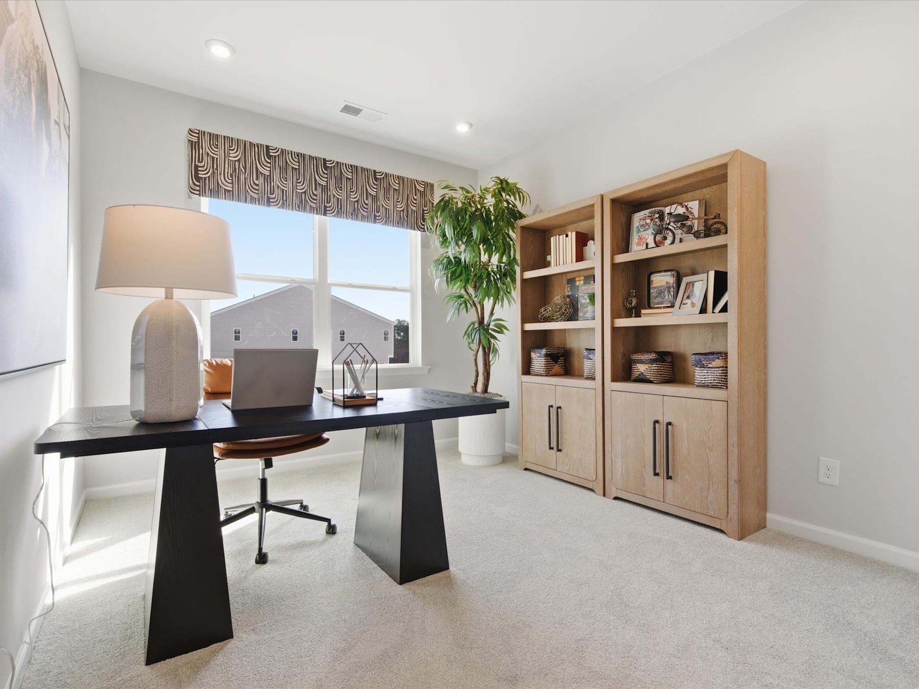 A modern and well-designed home office space with a sleek black desk, a wooden bookshelf unit, and a large window providing natural light.