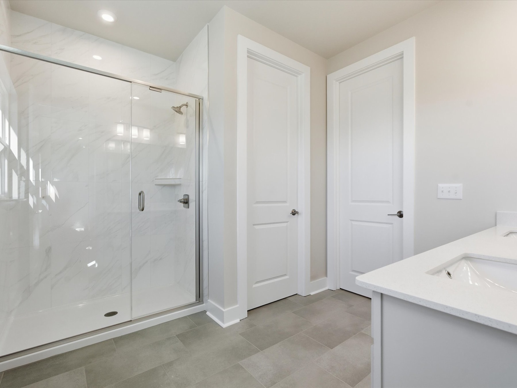 A bright, modern bathroom with a glass shower enclosure, white walls, and a vanity with a countertop.