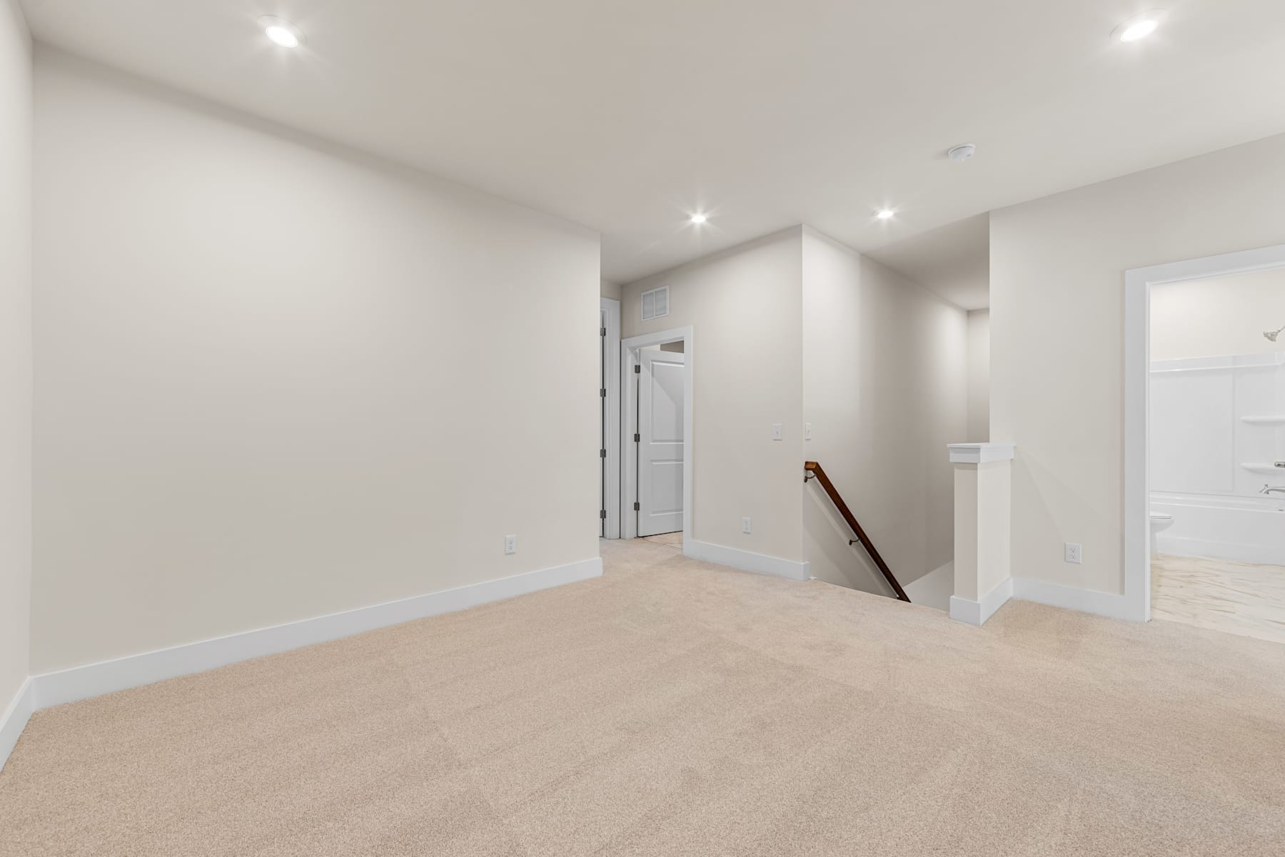 A bright, minimalist room with white walls, a hardwood floor, and recessed lighting, creating a clean and spacious atmosphere.