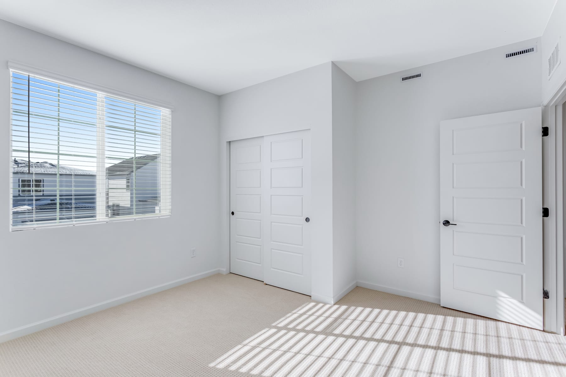 A bright, minimalist room with white walls, a large window, and two white doors leading to other areas of the space.