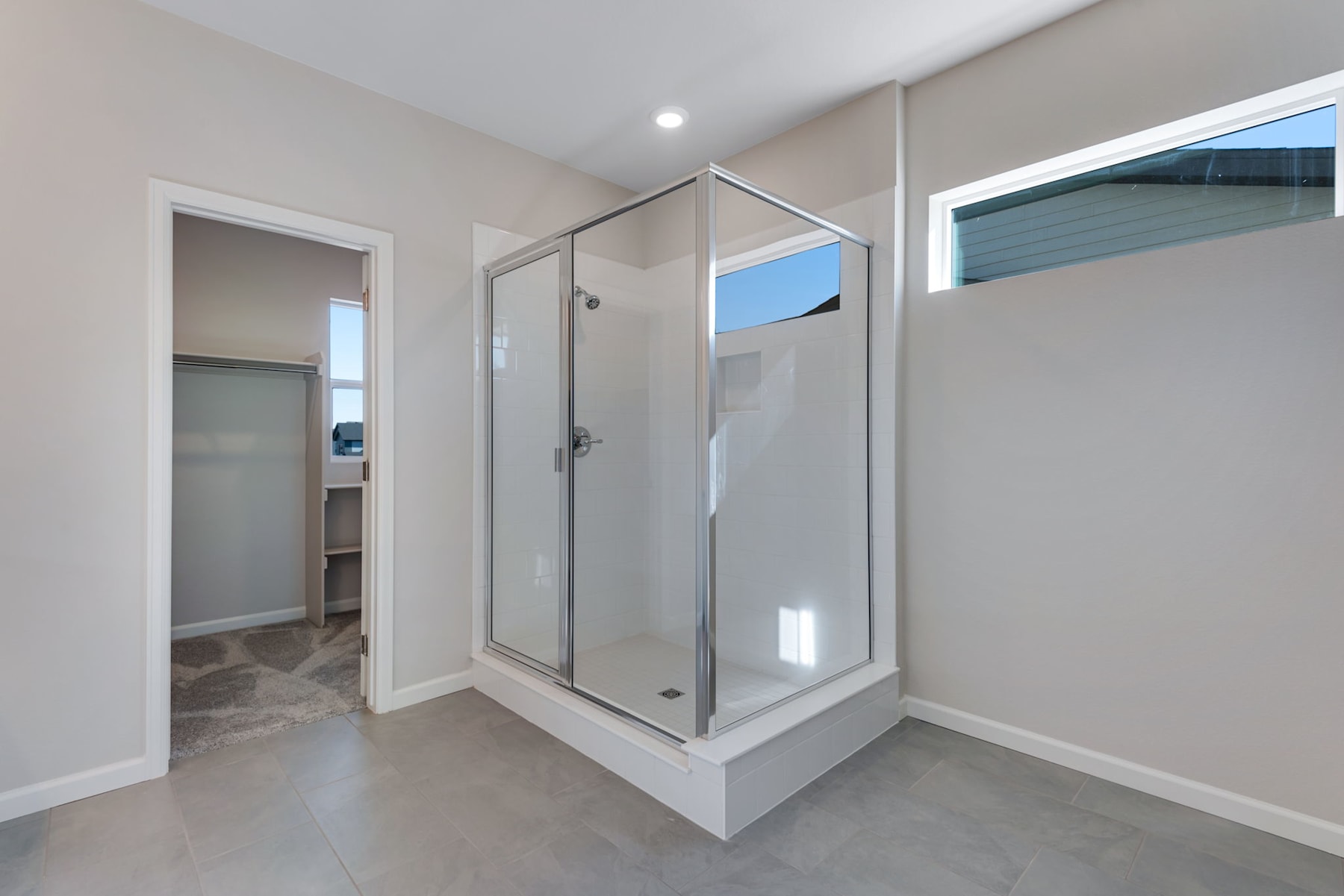 A modern, minimalist bathroom with a glass-enclosed shower stall, white walls, and a tiled floor.