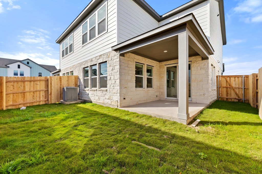 A newly constructed two-story house with a covered porch, surrounded by a lush green lawn and a wooden fence in the background.