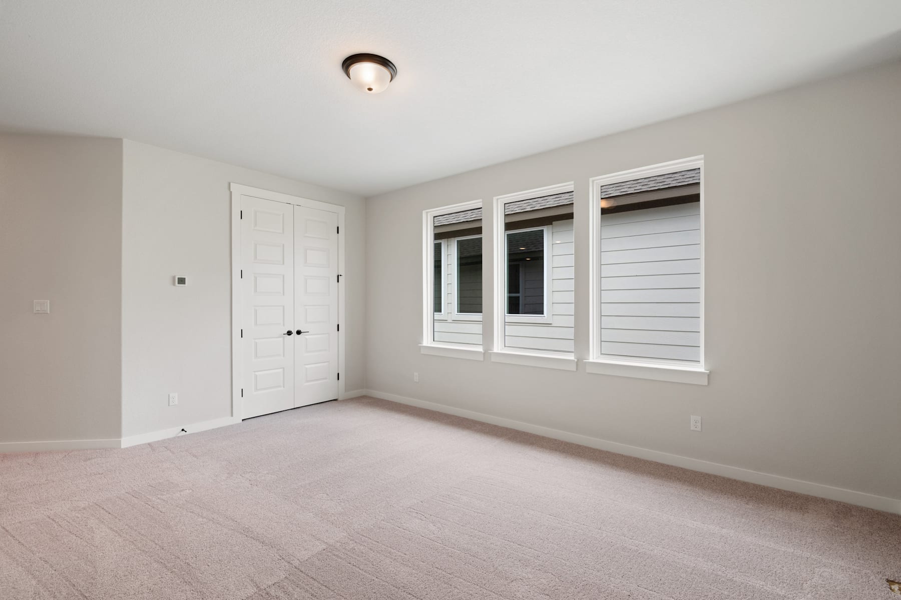 A simple, minimalist room with a white door, windows, and a ceiling light fixture, set against a neutral-colored wall and floor.
