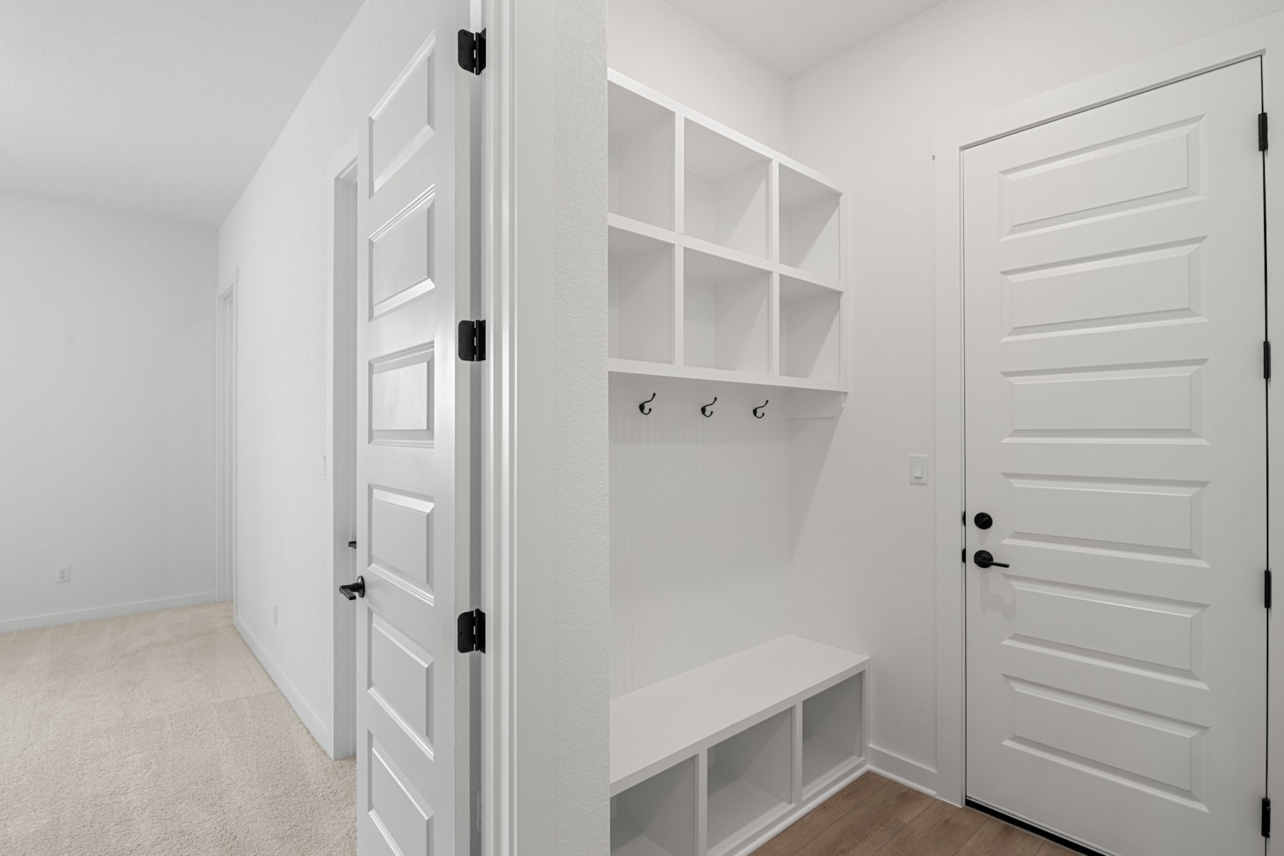 A bright, minimalist entryway with white walls, a built-in storage unit, and a wooden floor leading to a closed door.