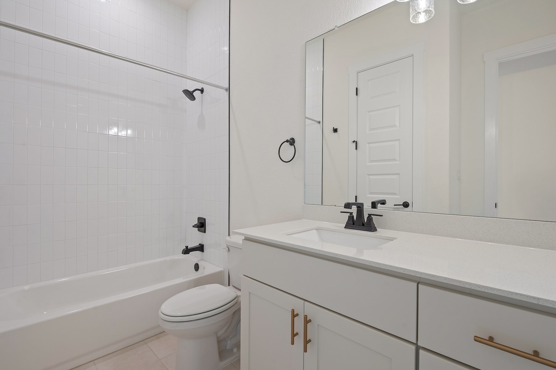 A modern, minimalist bathroom with a white vanity, toilet, and bathtub, illuminated by recessed lighting.