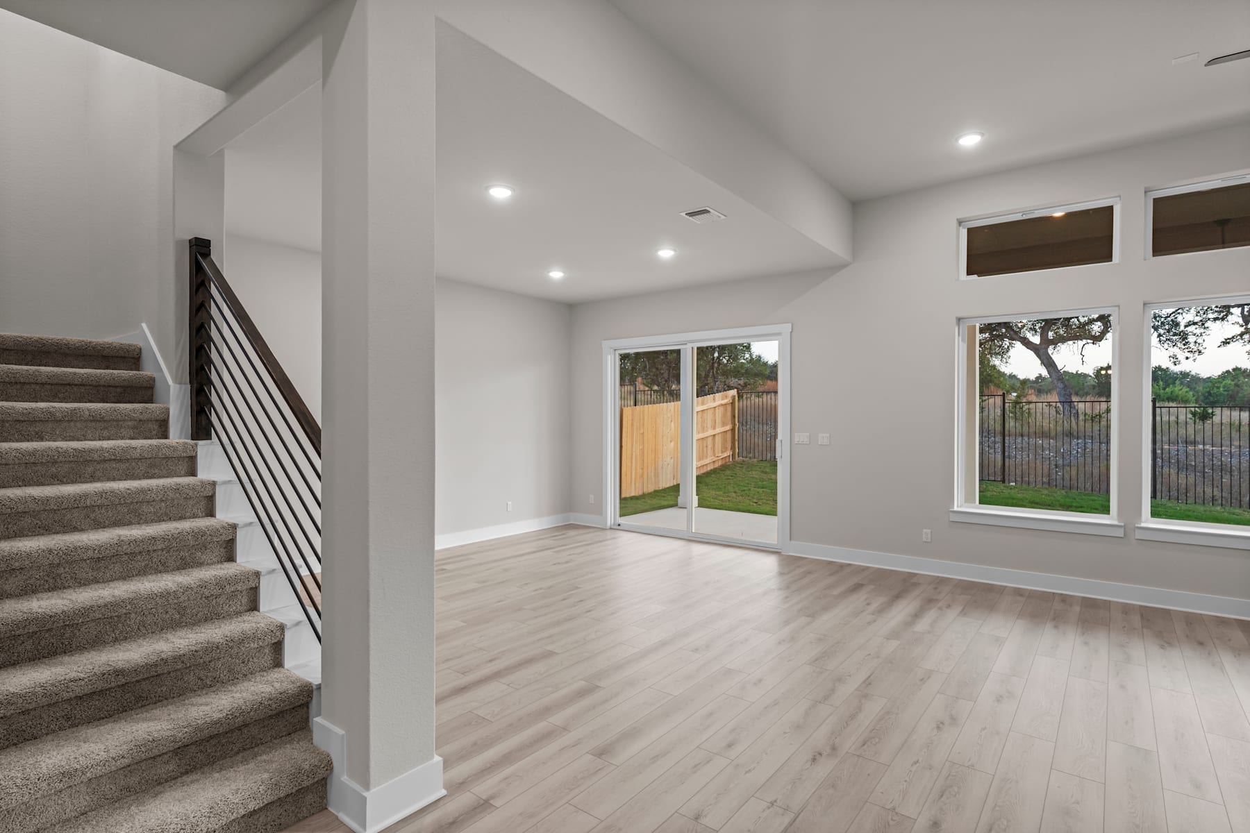 The image shows a spacious and bright interior with a staircase leading up to the second floor, and a sliding glass door that provides a view of the outdoor area.