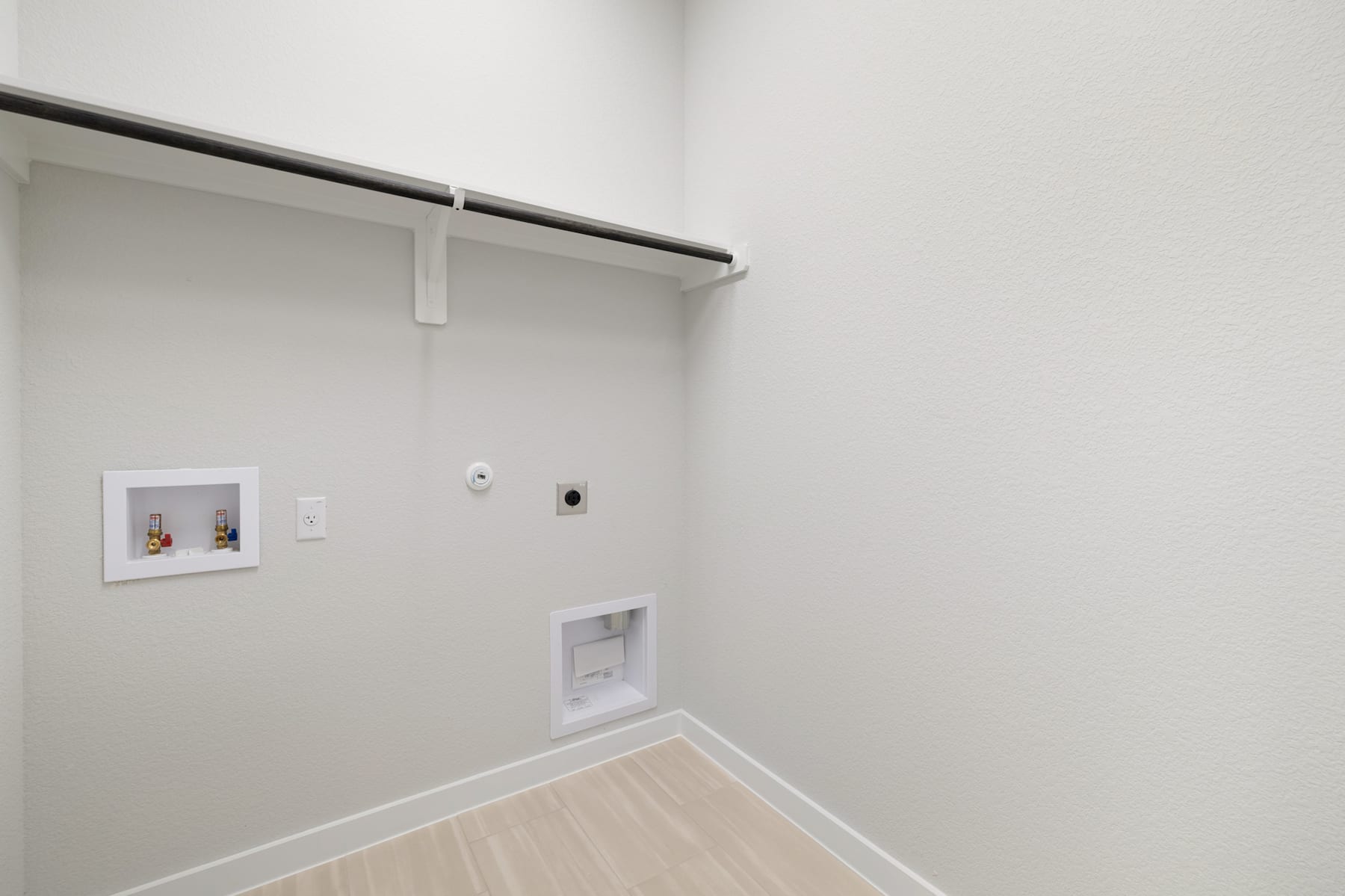 A simple, minimalist closet space with a white wall, a metal hanging rod, and a light-colored wooden floor.