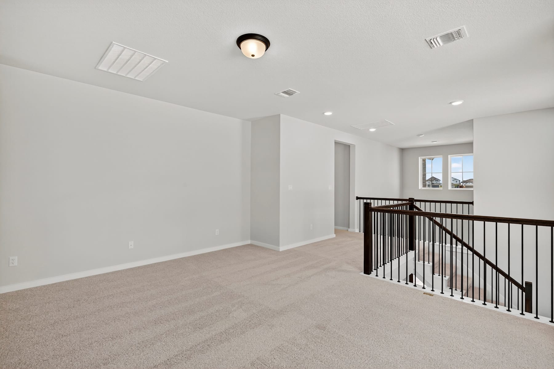 A spacious, well-lit room with a carpeted floor, a railing, and a ceiling light fixture.