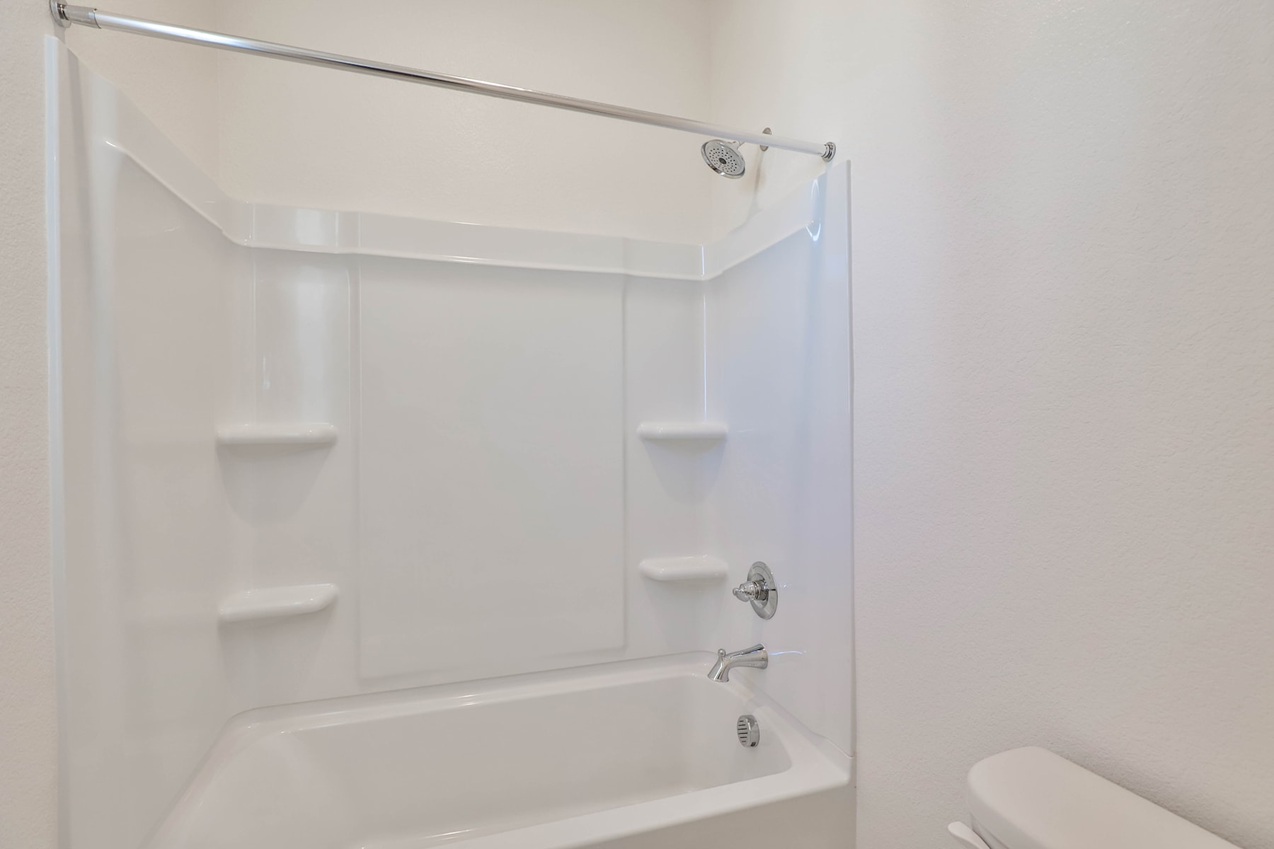 A white, tiled shower enclosure with a metal shower curtain rod and a white toilet visible in the background.