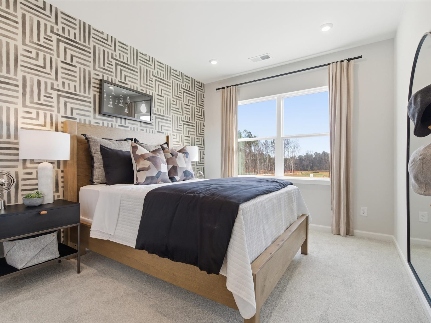 A modern and stylish bedroom with a patterned accent wall, a large bed with neutral bedding, and a window overlooking a scenic outdoor view.
