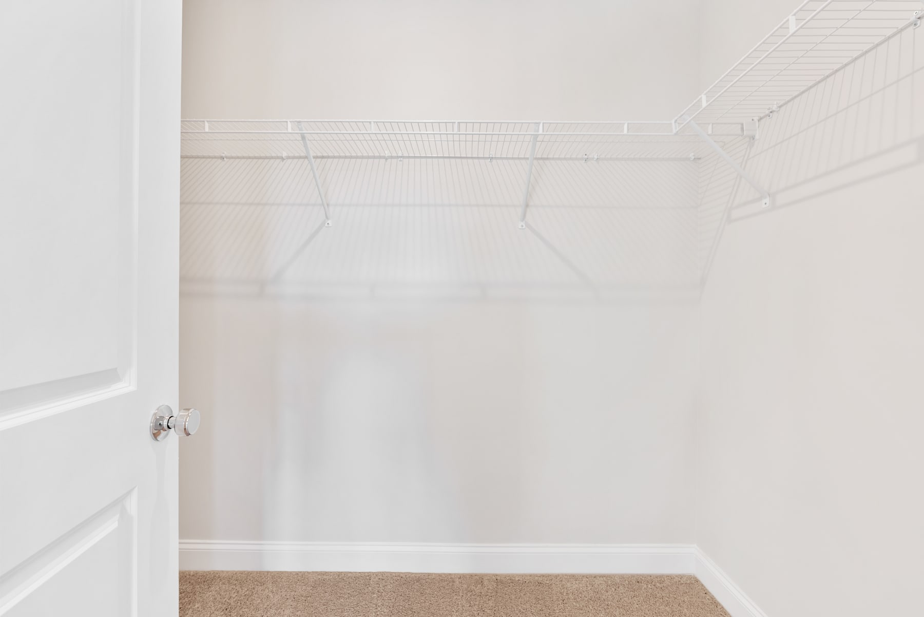 A simple, minimalist closet space with white walls, a metal clothing rod, and a beige carpeted floor.
