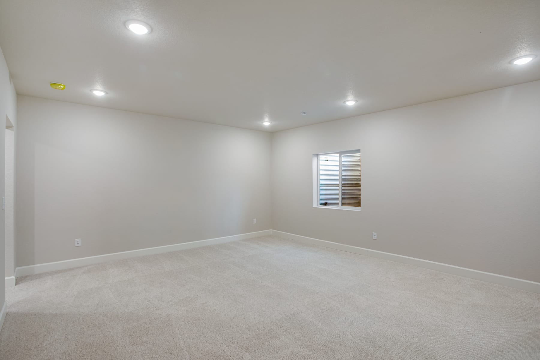 An empty, well-lit room with white walls, a window, and recessed lighting fixtures on the ceiling.