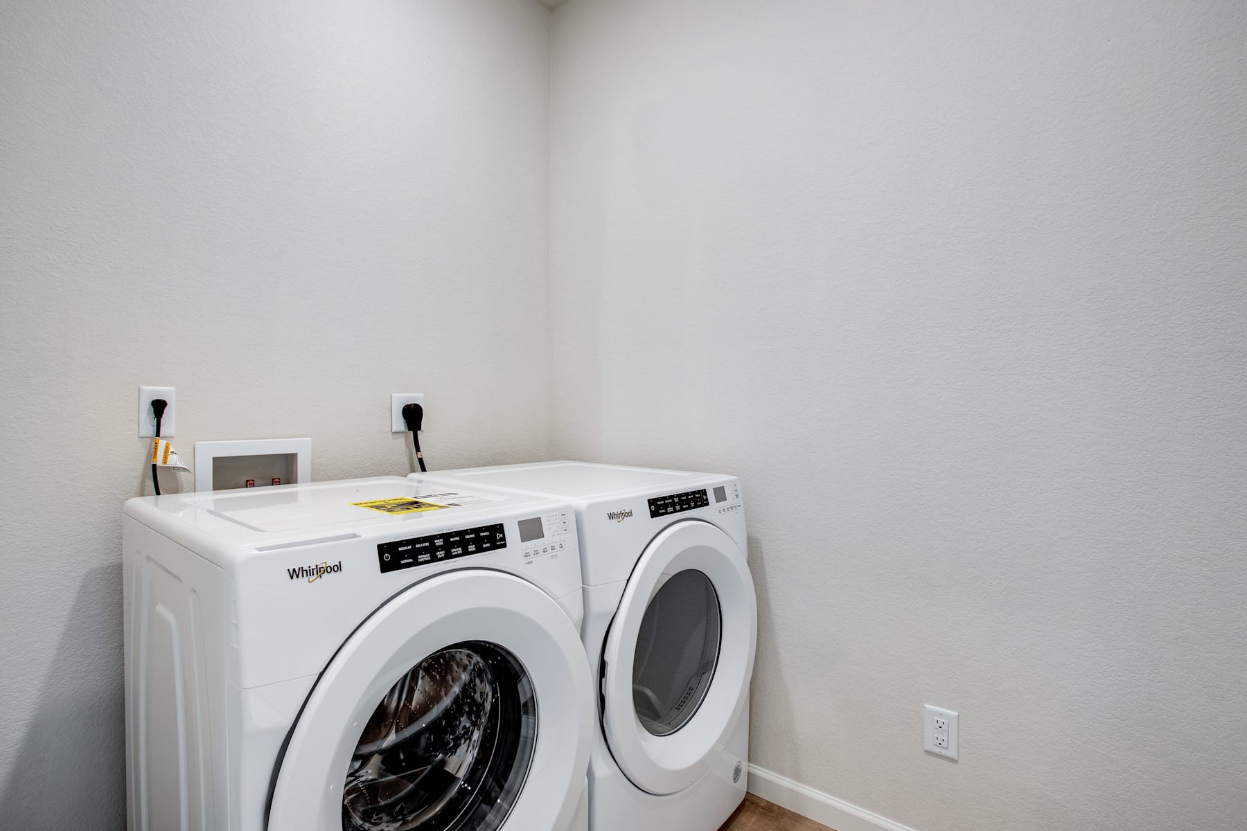 A white Whirlpool washing machine and dryer set against a plain white wall in a minimalist laundry room.