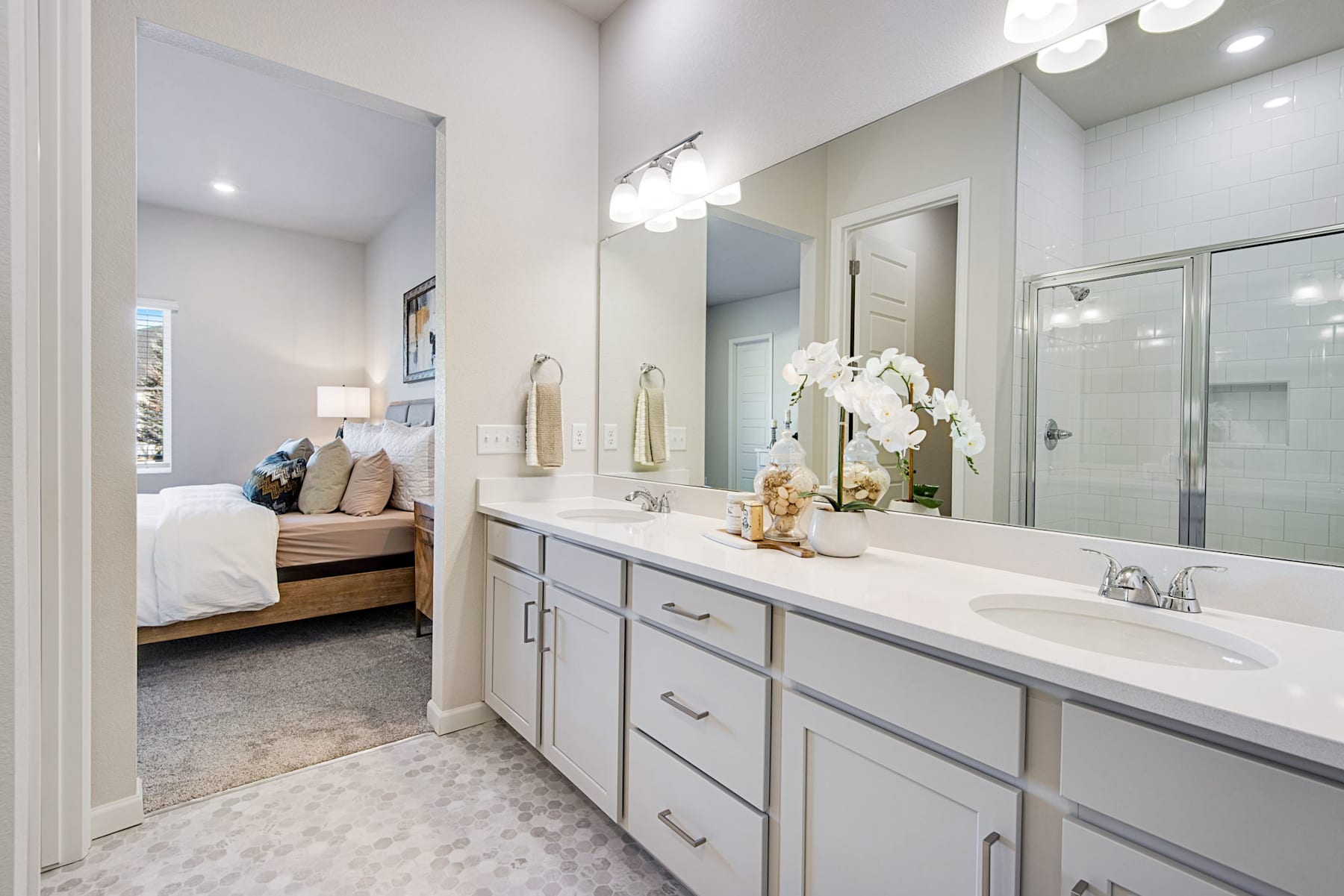 A spacious and well-lit bathroom with a large vanity, a mirror, and a bedroom visible in the background.