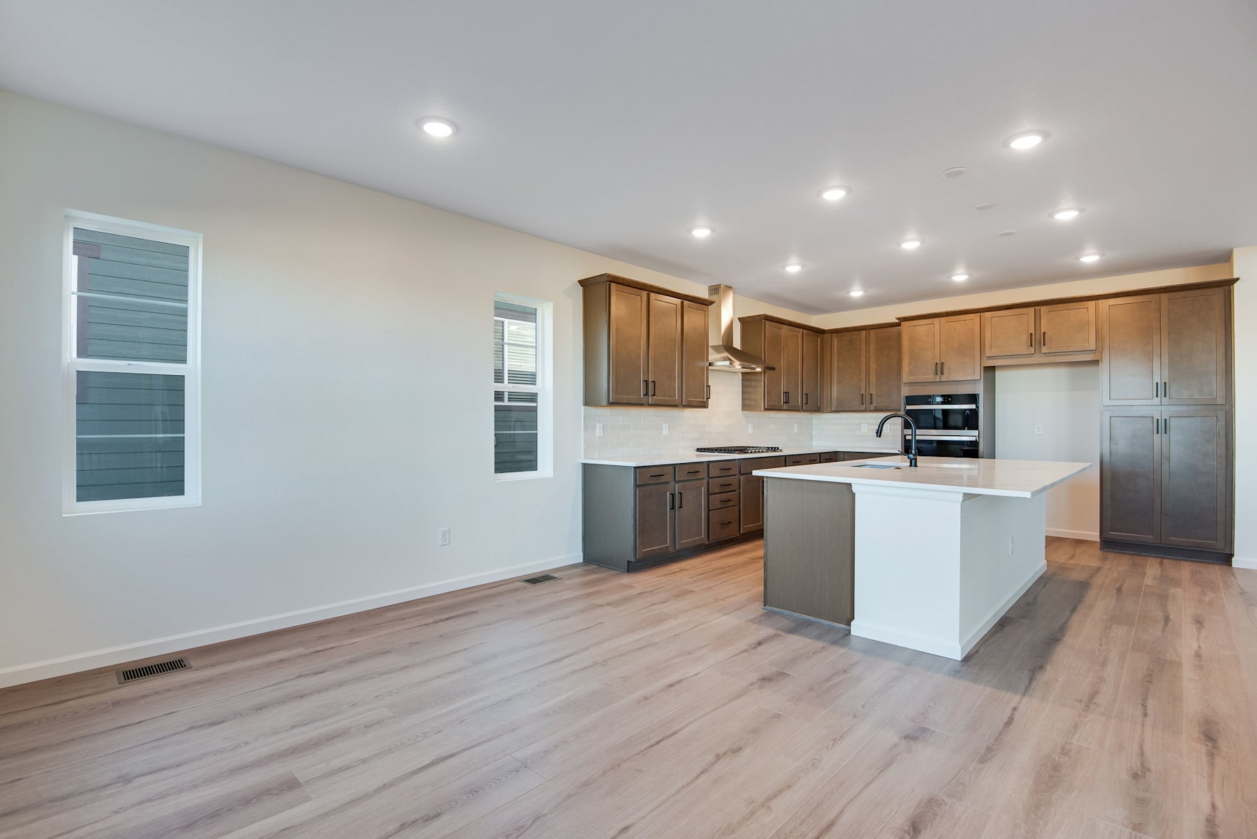 A modern, open-concept kitchen with wooden cabinets, white countertops, and hardwood flooring, illuminated by recessed lighting.