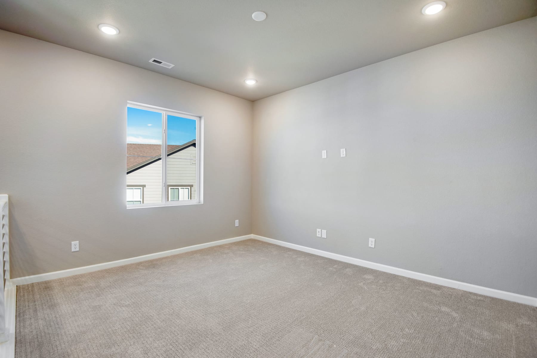 An empty room with white walls, a window, and a carpeted floor.