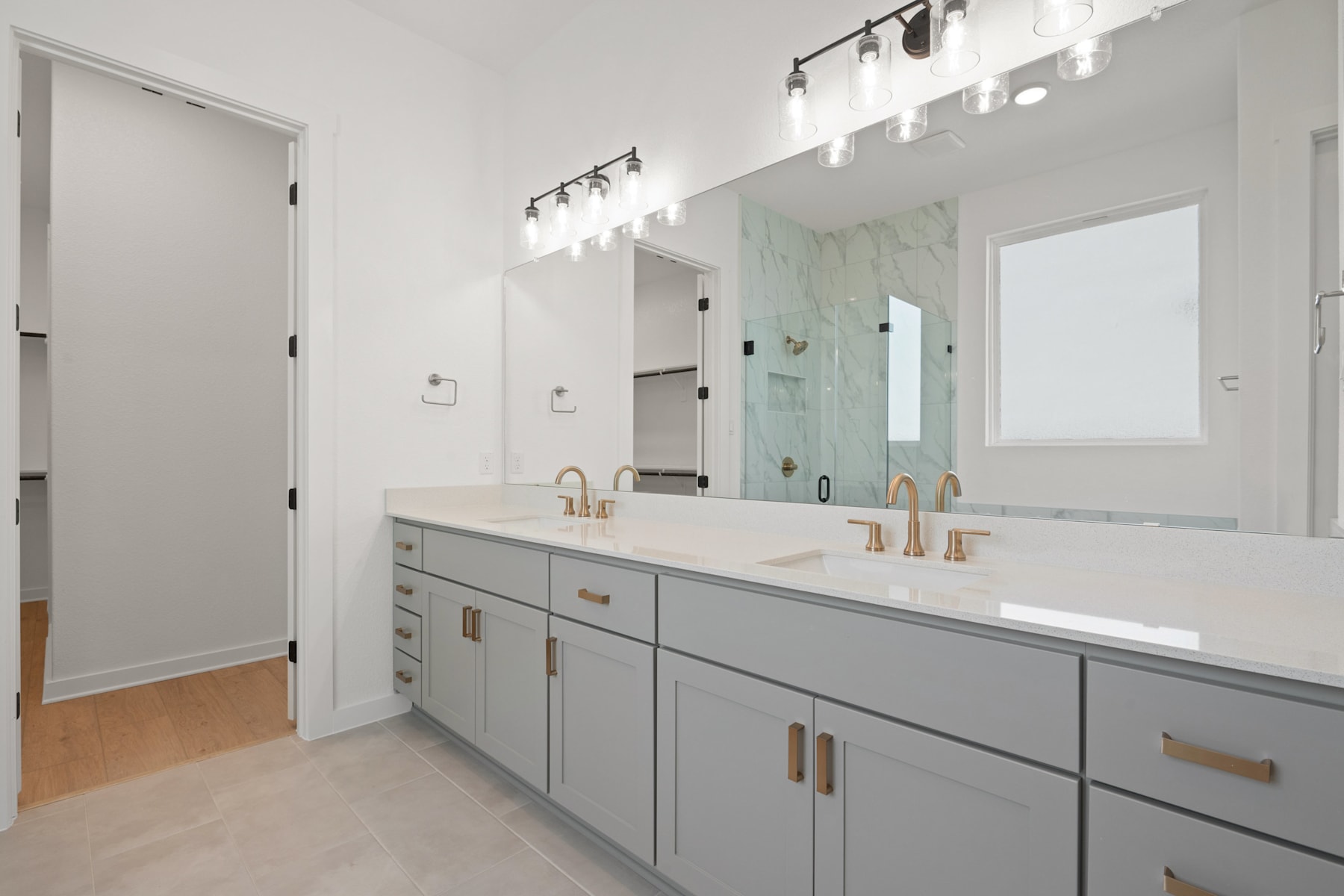 A modern and spacious bathroom with a double vanity, large mirrors, and track lighting fixtures, set against a neutral color palette.