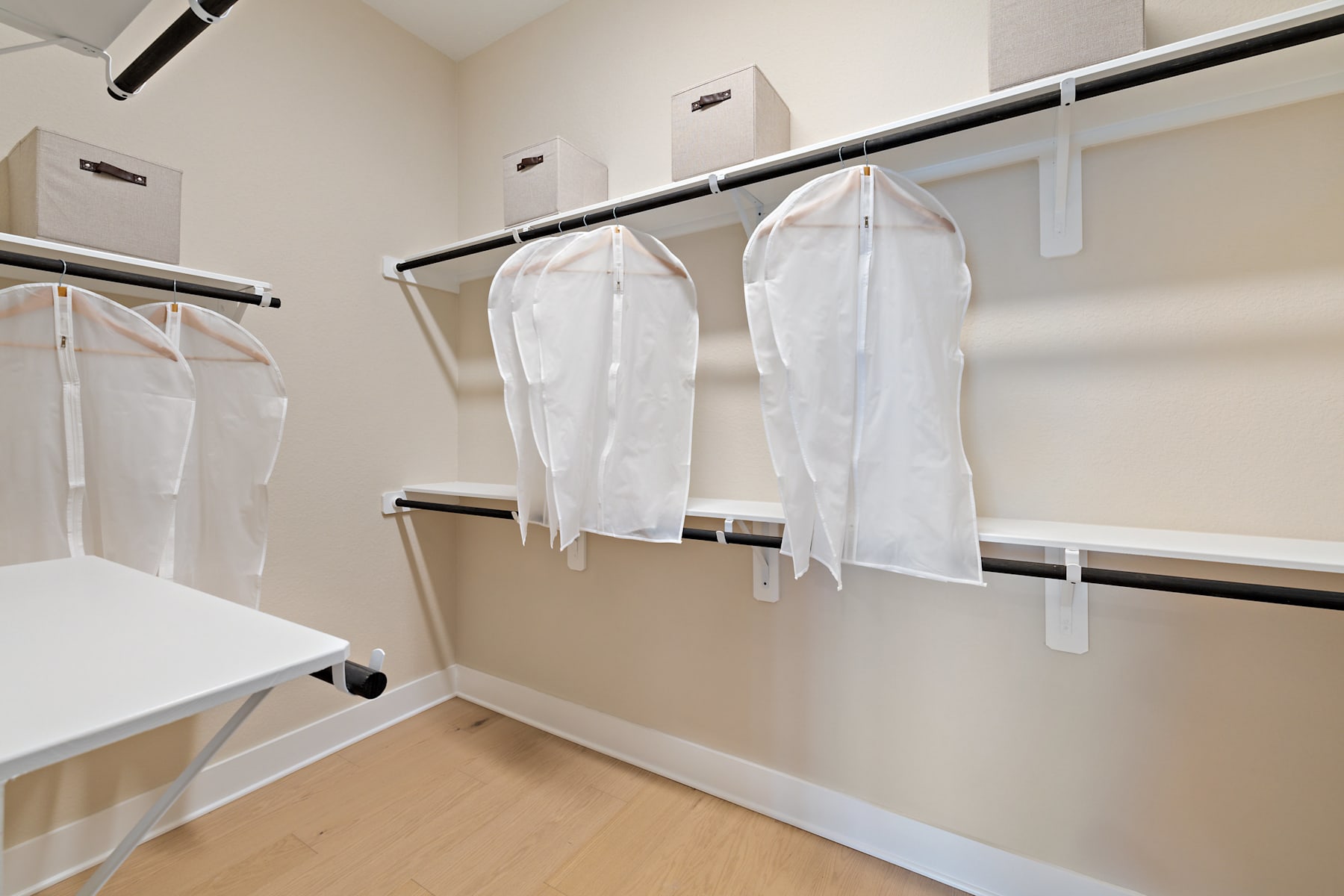 A well-organized closet with white garment bags hanging on metal rods, providing ample storage space and a clean, minimalist aesthetic.