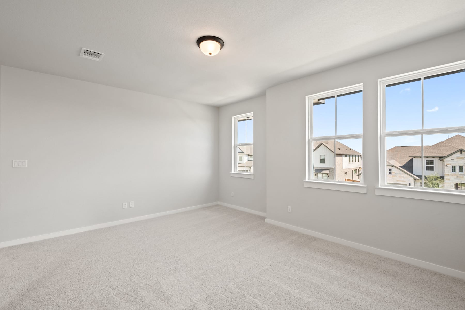 A bright, empty room with large windows overlooking a residential neighborhood in the background.