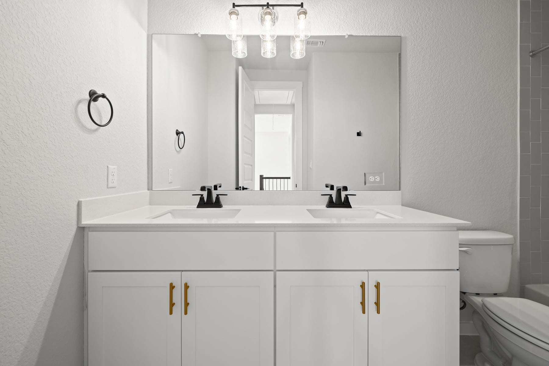 A modern, minimalist bathroom with a double vanity, white cabinets, and a large mirror above it, illuminated by a sleek light fixture.