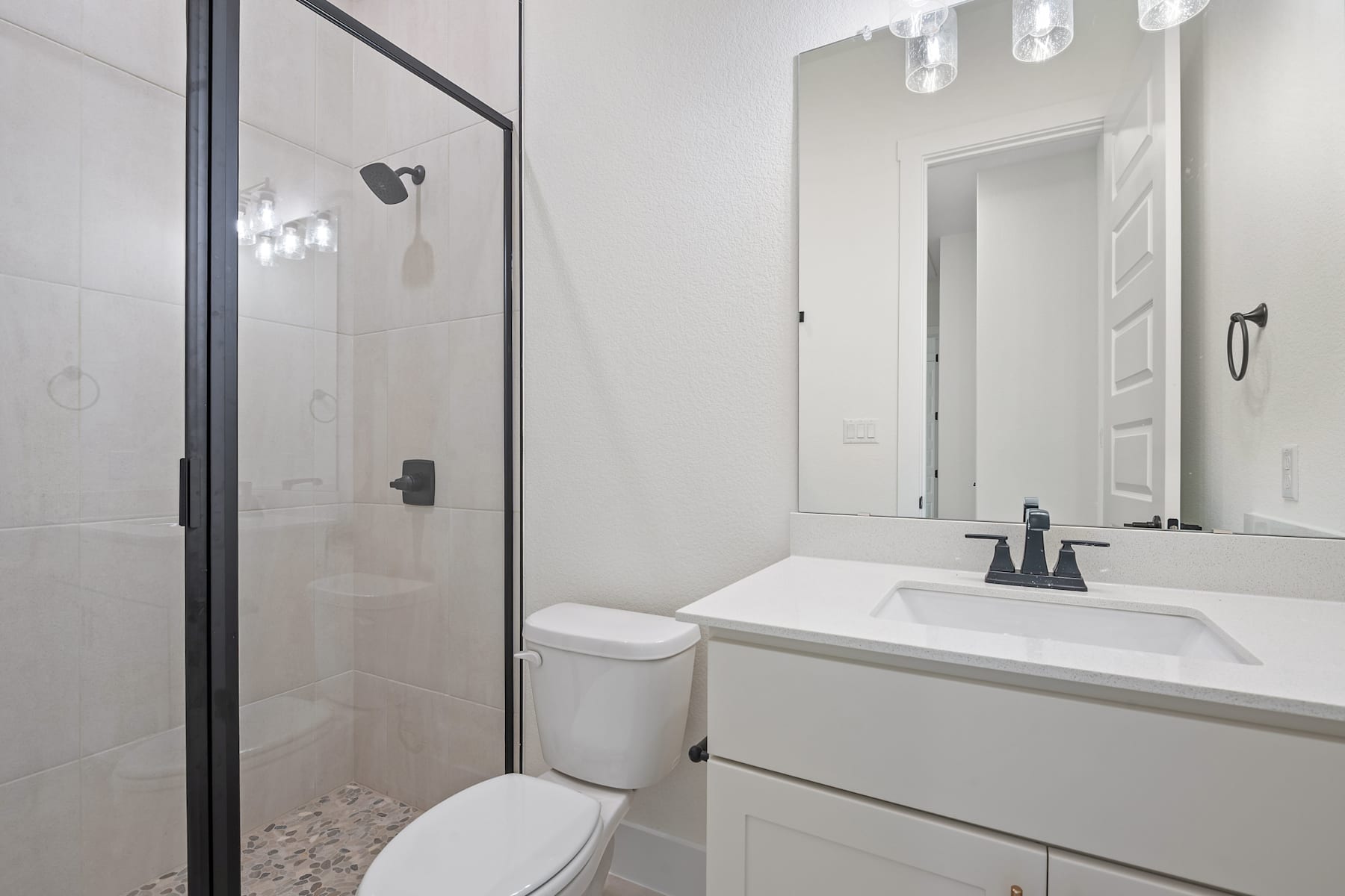 A modern, minimalist bathroom with a white vanity, a large mirror, and a glass-enclosed shower area.