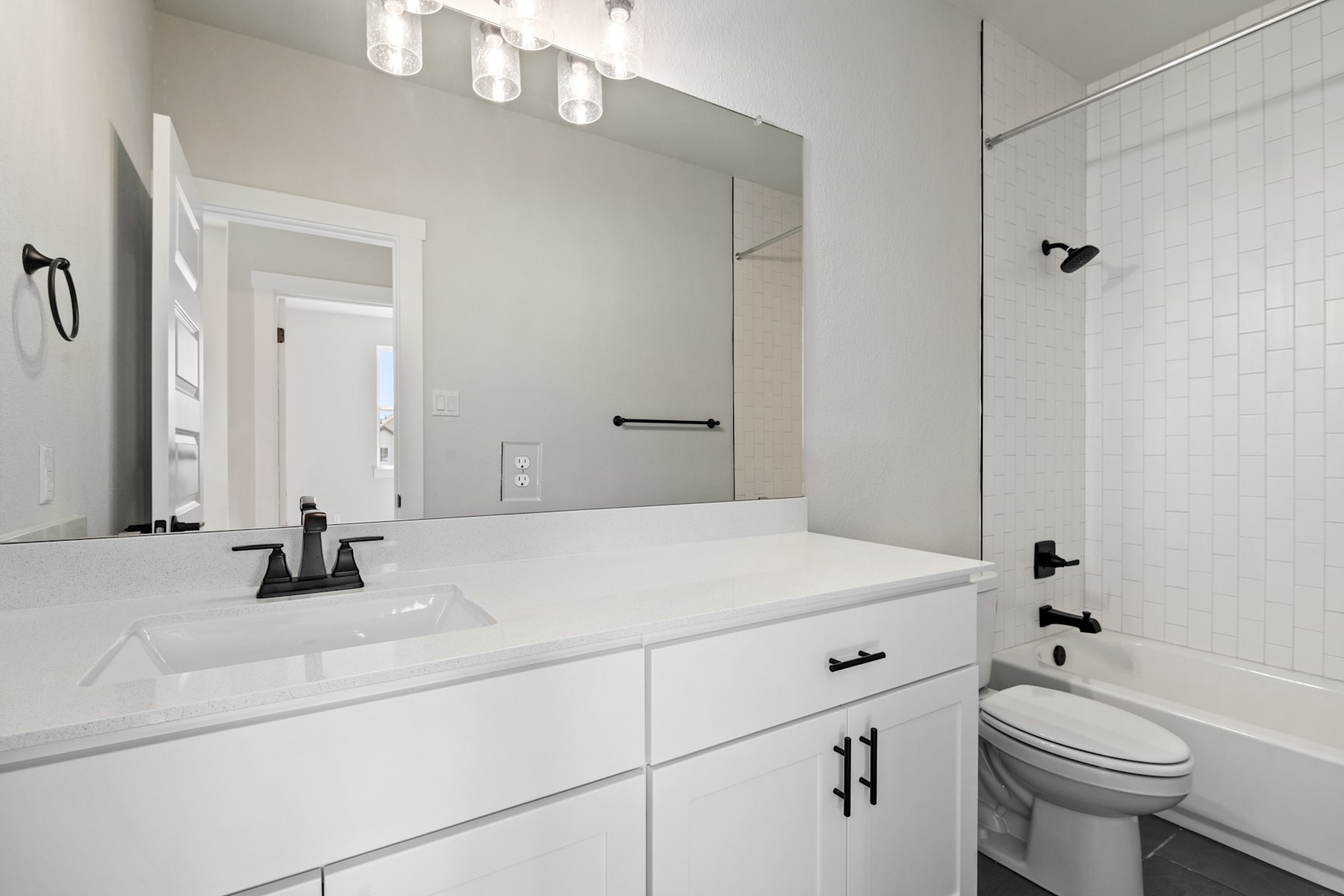 A modern, minimalist bathroom with a white vanity, a large mirror, and a sleek black and white color scheme.
