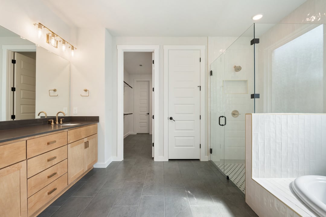 A modern and minimalist bathroom with a wooden vanity, white walls, and a glass shower enclosure.
