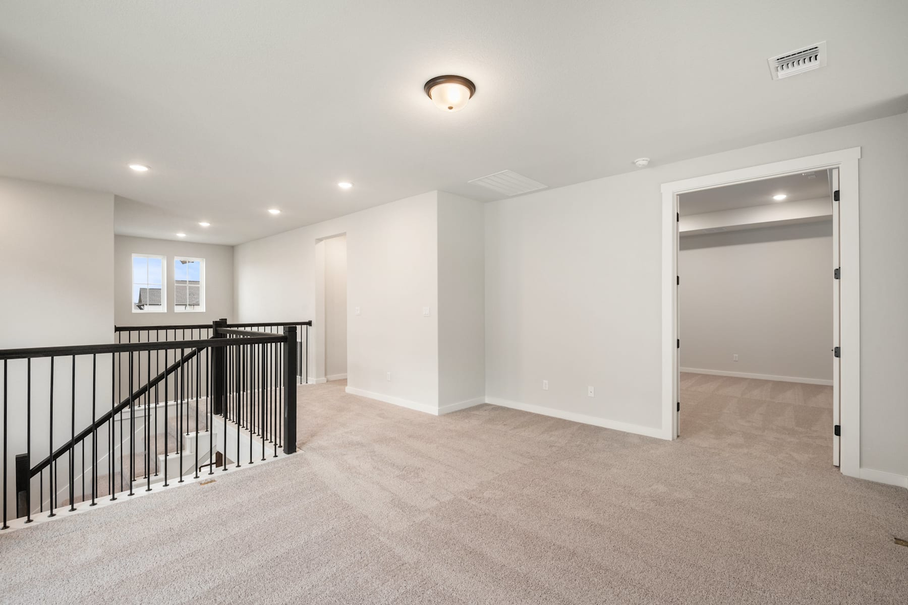 A spacious, well-lit hallway with a carpeted floor, a black metal railing, and a closed door leading to another room.