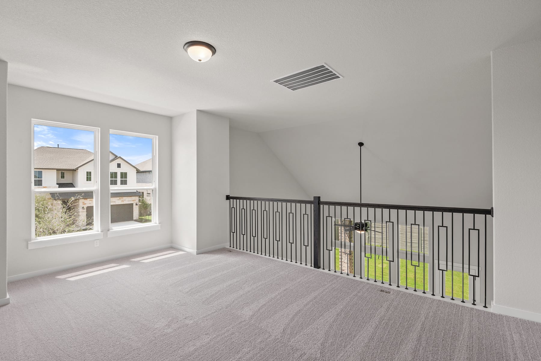 A bright, open room with a window overlooking a residential neighborhood, featuring a metal railing and a ceiling light fixture.