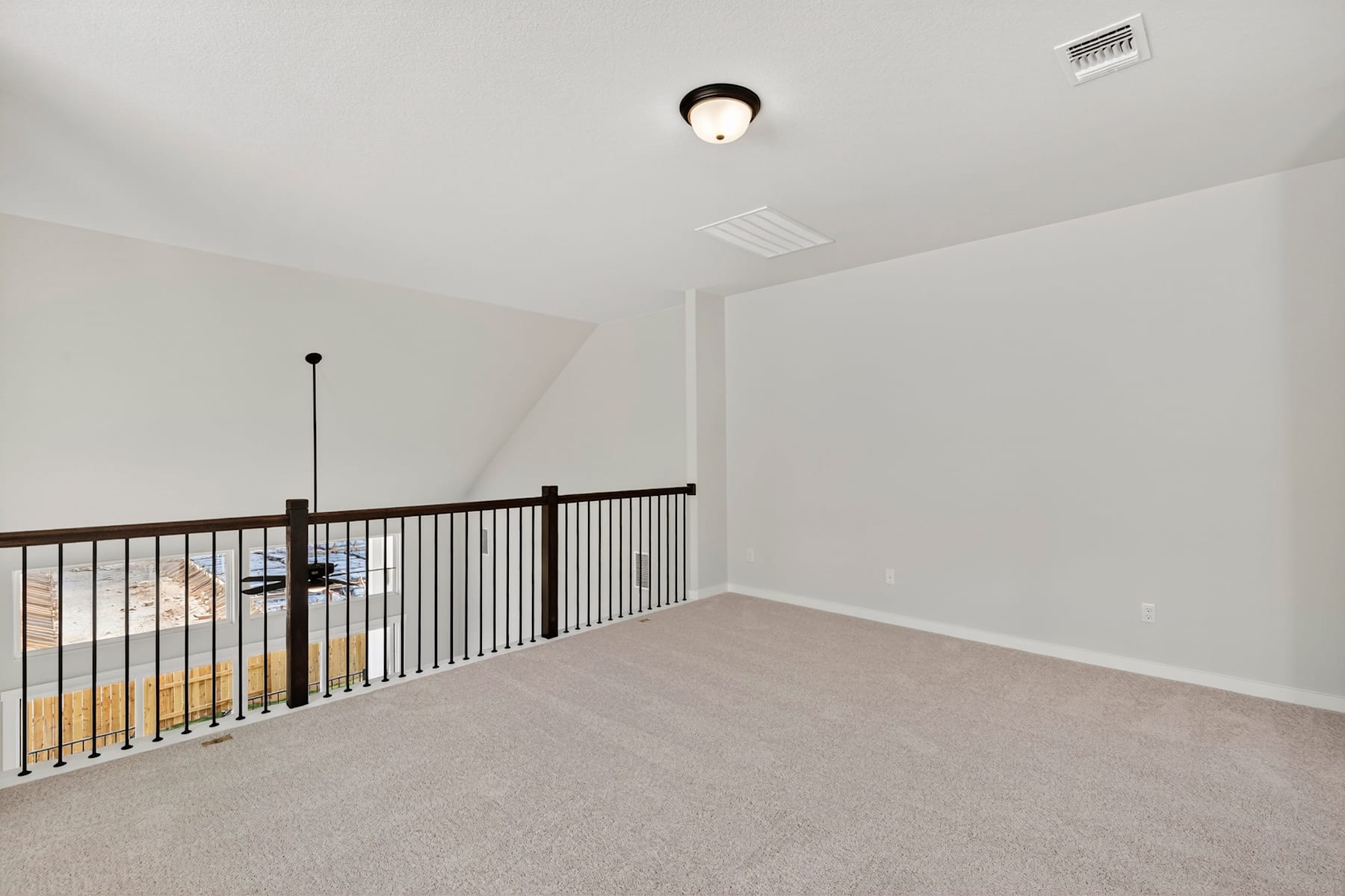An empty room with a carpeted floor, a railing, and a ceiling light fixture.