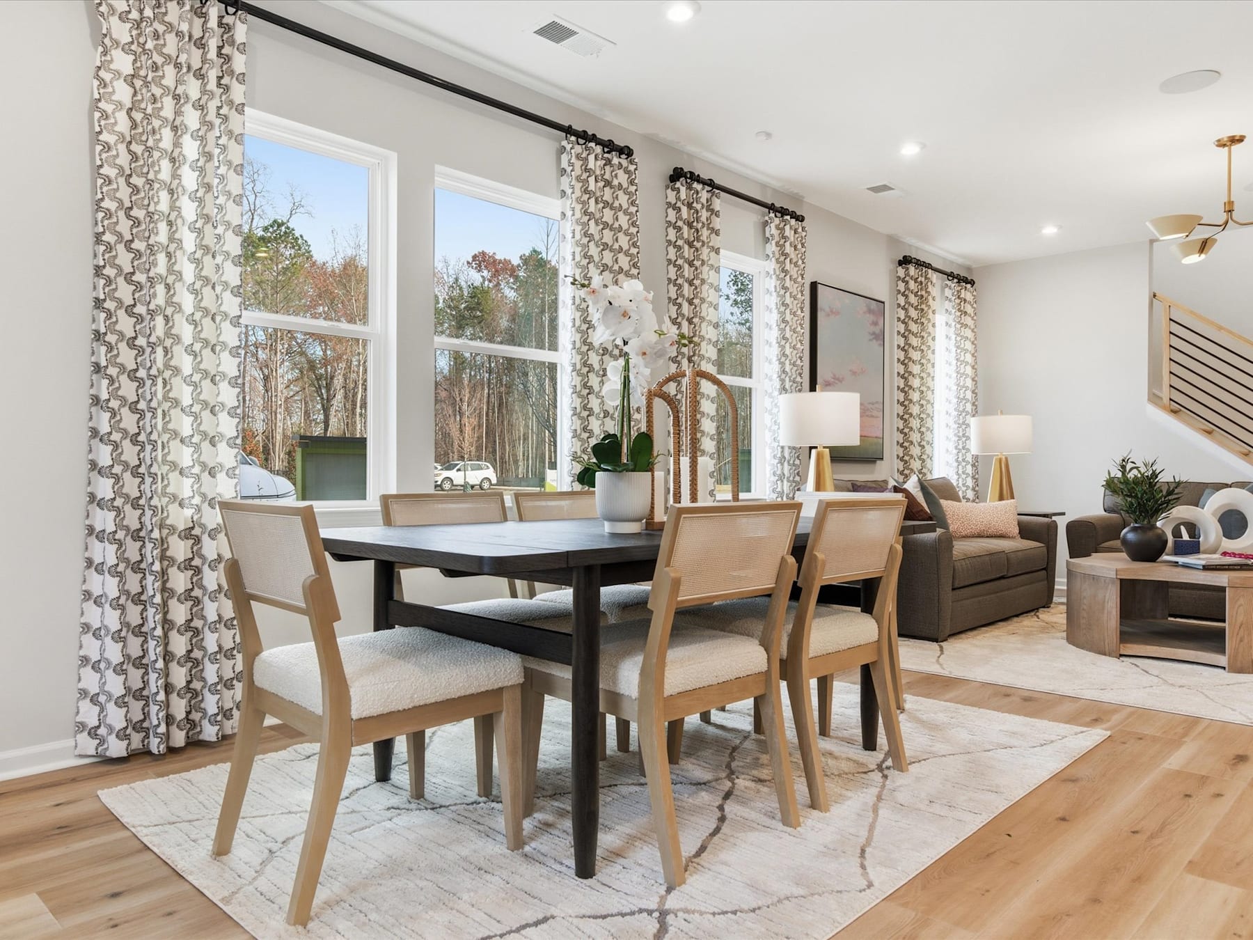 A modern and cozy dining room with a wooden table, upholstered chairs, and large windows overlooking a scenic outdoor view.