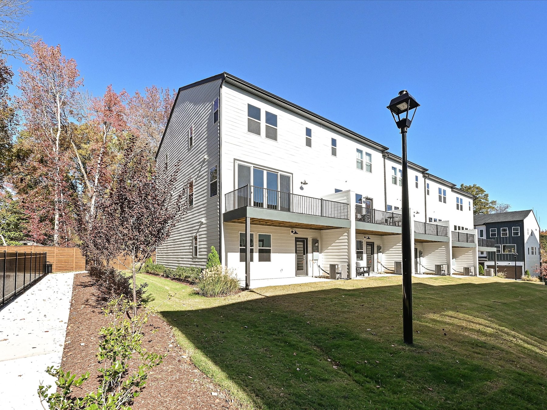 A multi-story residential building with a grassy lawn and landscaping in the foreground, set against a clear blue sky with trees in the background.
