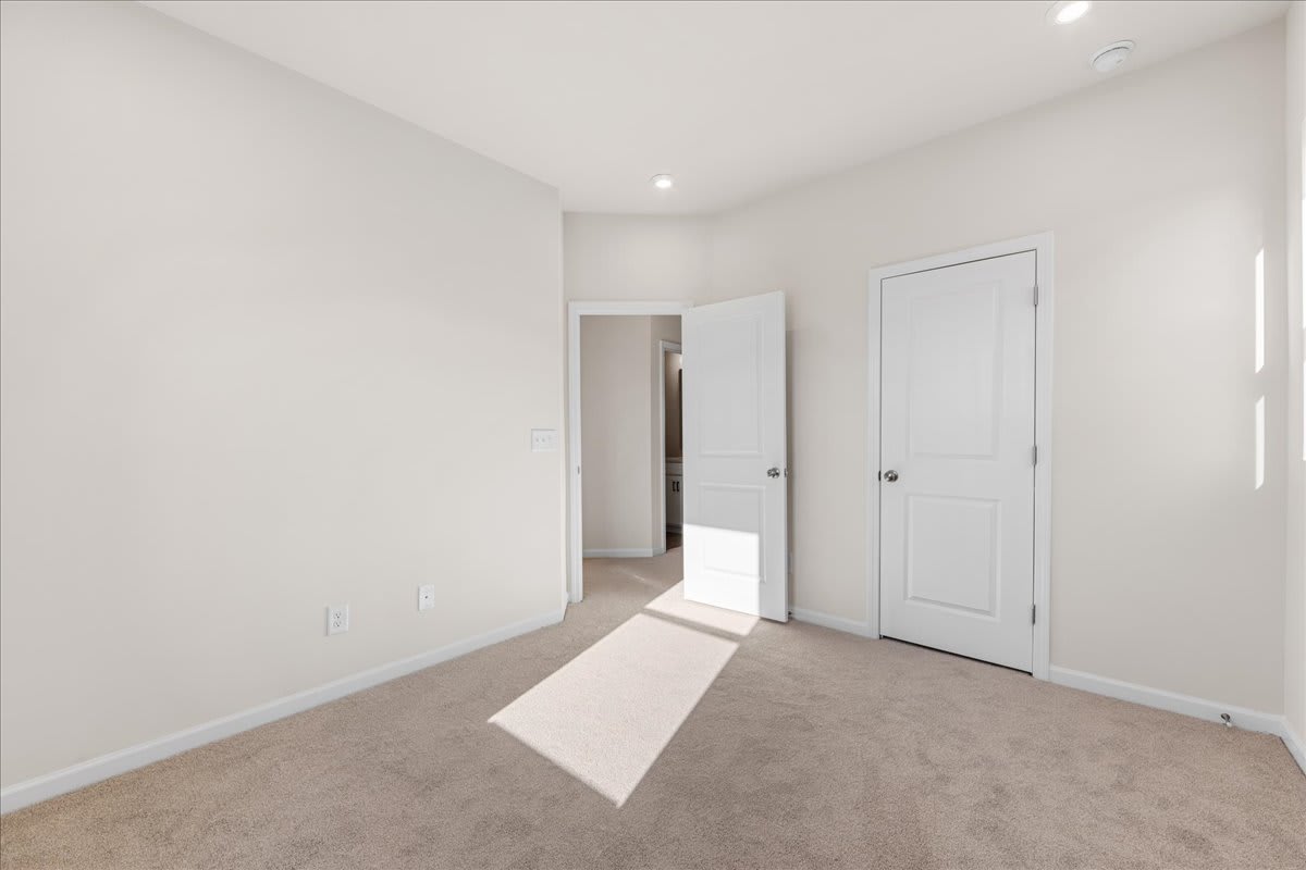 A bright, minimalist room with white walls, a carpeted floor, and two closed doors leading to other areas.