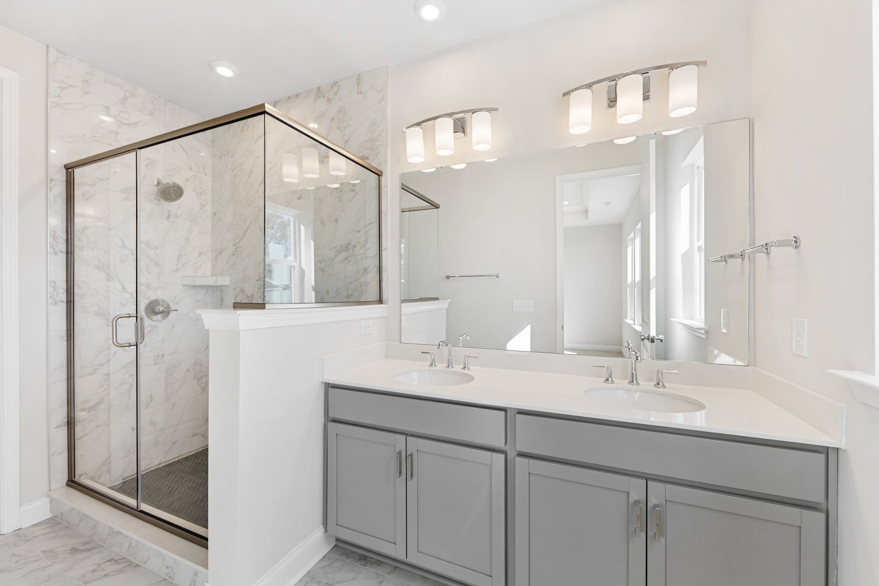 A modern, well-lit bathroom with a glass-enclosed shower, a vanity with gray cabinets, and a large mirror on the wall.