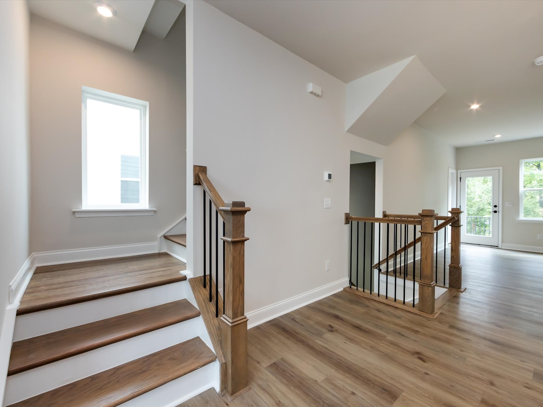 A bright and spacious entryway with wooden stairs, a railing, and hardwood floors leading to a hallway with natural lighting.