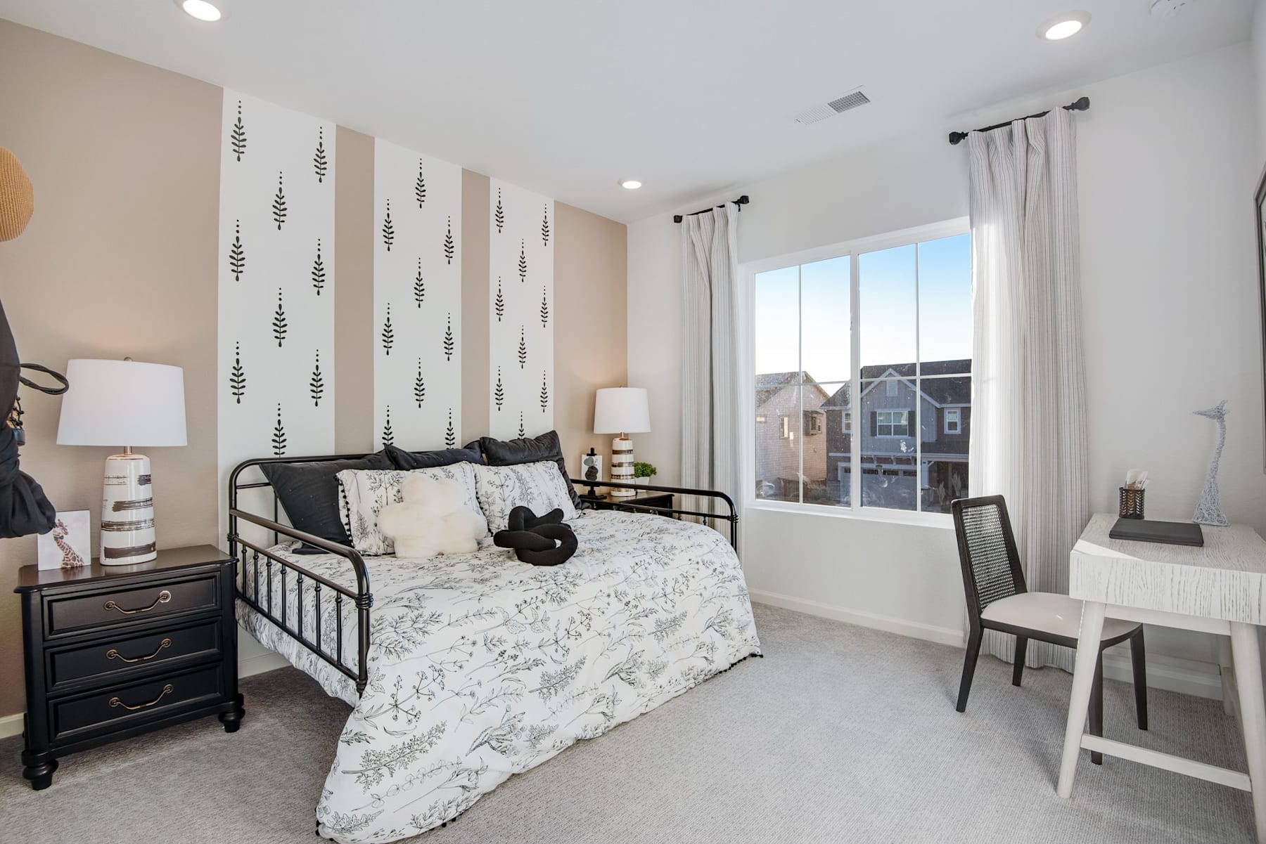 A cozy and well-decorated bedroom with a metal bed frame, patterned bedding, and a desk area near the window, creating a comfortable and inviting living space.