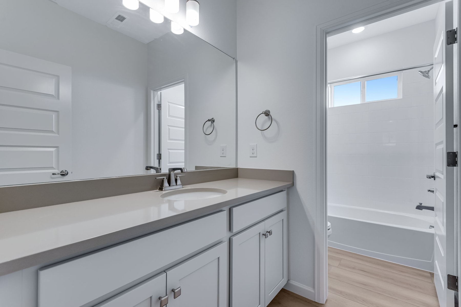 A modern, well-lit bathroom with a vanity, mirror, and a bathtub visible in the background.