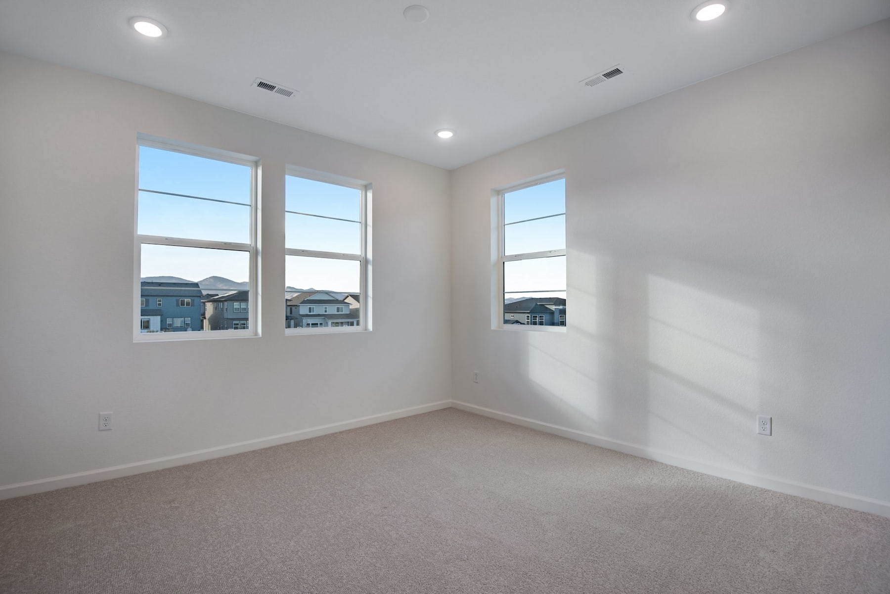 An empty, well-lit room with large windows overlooking a residential neighborhood.