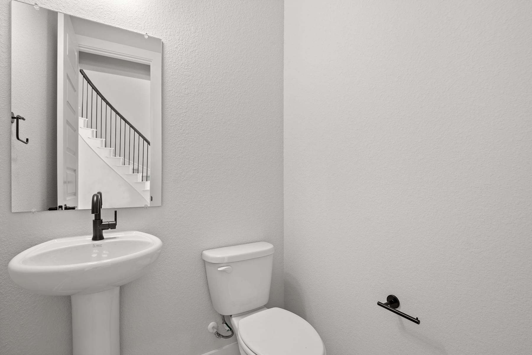 A simple and minimalist bathroom with a white pedestal sink, a toilet, and a framed mirror on the wall.