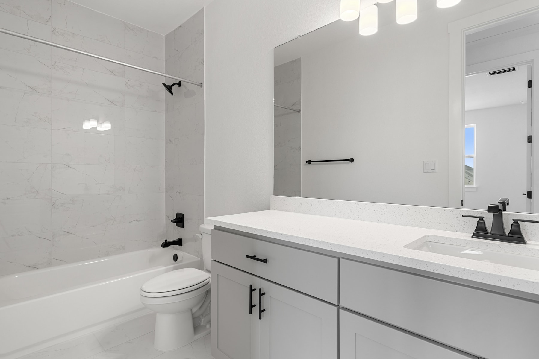 A modern, minimalist bathroom with a white vanity, a large mirror, and a bathtub visible in the background.