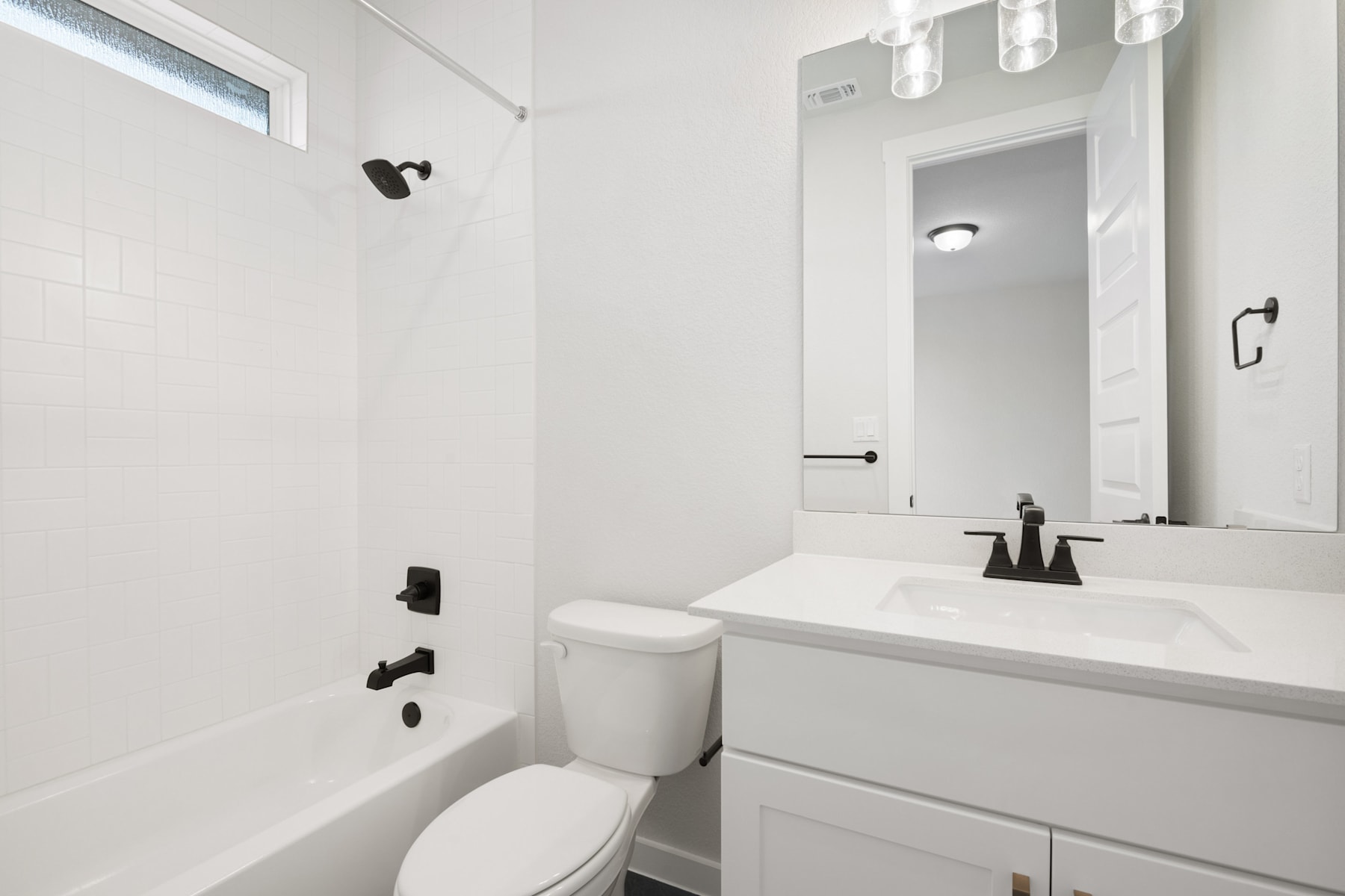 A modern, minimalist bathroom with a white vanity, toilet, and tiled walls, featuring black hardware and lighting fixtures.