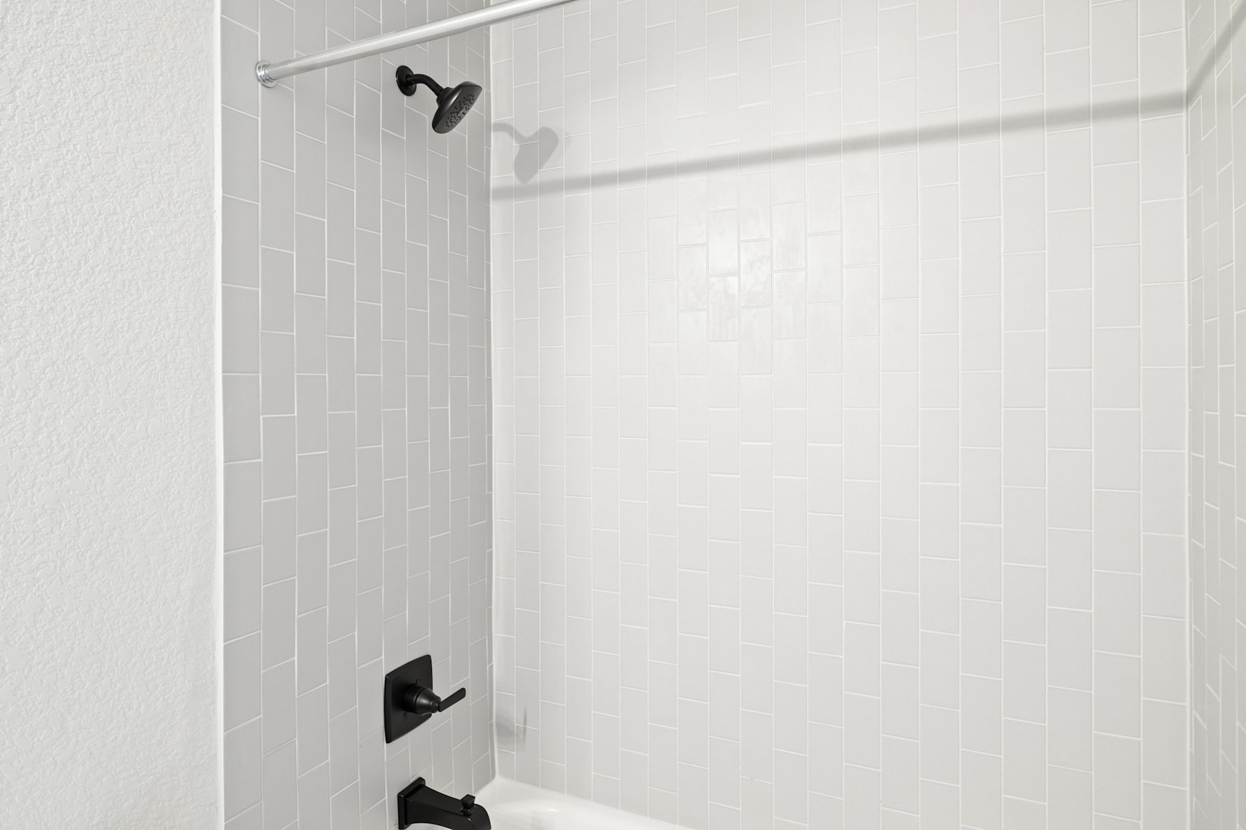 A minimalist bathroom interior with white tiles and a black shower fixture.